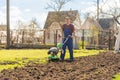 A farmer in the garden tills the land with a motorized cultivator or power tiller, preparing the soil for planting crops Royalty Free Stock Photo