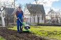 A farmer in the garden tills the land with a motorized cultivator or power tiller, preparing the soil for planting crops Royalty Free Stock Photo