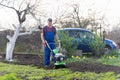 A farmer in the garden tills the land with a motorized cultivator or power tiller, preparing the soil for planting crops Royalty Free Stock Photo