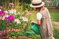 Farmer girl in summer straw hat. Little gardener farming, watering flowerbed with pink flowers, having fun in garden. Big green Royalty Free Stock Photo