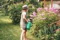 Farmer girl in summer straw hat. Little gardener farming, watering flowerbed with pink flowers, having fun in garden. Big green Royalty Free Stock Photo