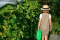 Farmer girl in summer straw hat. Little vegetables gardener farming in garden. Big green watering can water fresh Royalty Free Stock Photo