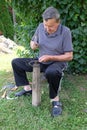 Farmer with hammer and iron tool on the tree stump is sharpening his scythe