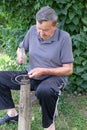 Farmer with hammer and iron tool on the tree stump is sharpening his scythe