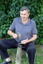 Farmer with hammer and iron tool on the tree stump is sharpening his scythe