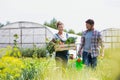 Farmer holding organic produce in wooden box on her farm with gardener holding watering can next to her