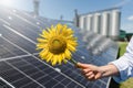 Farmer holds sunflower on a background of solar panel and agricultural silos Royalty Free Stock Photo