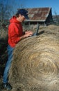 Farmer with laptop computer on hay bale