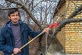 Farmer man with garden saw for cutting branches of cherry bush overgrown with lichen. Pruning of fruit trees with lopper. Spring Royalty Free Stock Photo