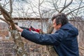 Farmer man with garden saw for cutting branches of cherry bush overgrown with lichen. Pruning of fruit trees with lopper. Spring Royalty Free Stock Photo