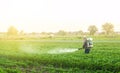 A farmer with a mist sprayer blower processes the potato plantation from pests and fungus infection. Harvest processing.