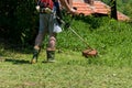 Man cutting tall grass with hand lawn mower in garden on summer day