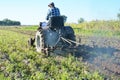 Farmer on old handmade tractor plowing on potatoes field.