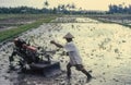 A farmer ploughs a rice paddy field with an iron buffalo mechanical cultivator in Bali Indonesia. Retro slide film capture