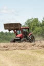 A farmer in a red tractor hays a field in New England