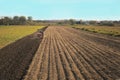 A farmer on a red tractor with a seeder sows grain in plowed land in a private field in the village area. Mechanization of spring