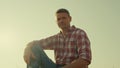 Farmer resting sunlight field at clear sky. Tired agriculture worker posing