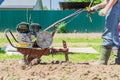 Farmer in rubber boots and blue jeans plows a soil with smal motor tractor Royalty Free Stock Photo