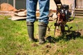 Farmer in rubber boots and blue jeans plows a soil with smal motor tractor Royalty Free Stock Photo
