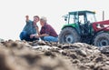 Farmer showing field while examining soil with senior farmer at farm against tractor