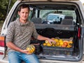 Farmer sits on the trunk of a car with crop of autumn pumpkin