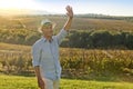 Winemaker smiling and waving hand in front of sunset at grape yards