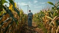 A farmer stands in the middle of his field surrounded by tall stalks of corn. In the background a wind turbine can be Royalty Free Stock Photo