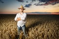 Farmer in a straw hat and glasses standing in a ripe wheat field before sunset