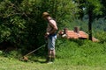 Farmer trimming tall grass in backyard with gasoline mower on hot summer day