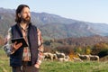 Farmer with tablet on the background of a flock of sheep.