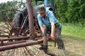 Farmer tractor-driver, repairing old tractor hay rake in mown me