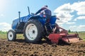 Farmer on a tractor with a milling machine processes loosens soil in the farm field. Preparation for new crop planting. Grind