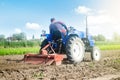 Farmer on a tractor with a milling machine processes loosens soil in the farm field. Preparation for new crop planting. Loosening