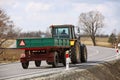 A farmer on a tractor pulls a trailer along an asphalt road passing among green fields. Rear view of multi-purpose agricultural Royalty Free Stock Photo