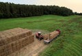 Farmer unloading round bales of straw from Hay Trailer with a front end loader. Store hay at farm. Hay rolls as Forage feed for