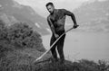 Farmer using scythe. Farmer with a scythe on green grass field. Muscular Farmer cut grass. Rural farmer on summer meadow