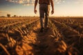 A farmer walking across a field of dry, cracked earth, a shovel over his shoulder-