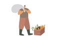 A farmer in work clothes and boots with a bagful on his back is standing near a crate of carrots.