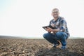 Farmer works in field in spring with tablet. An elderly farmer looks at tablet and green shoots. A smart, agronomist