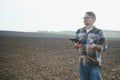 Farmer works in field in spring with tablet. An elderly farmer looks at tablet and green shoots. A smart, agronomist