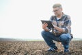 Farmer works in field in spring with tablet. An elderly farmer looks at tablet and green shoots. A smart, agronomist