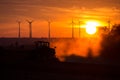 Farmers working with a tractor on the field at sunset with wind turbines in the background Royalty Free Stock Photo