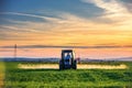 Farming tractor plowing and spraying on field, sunset