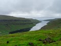 Faroe Islands. The bay cutting into the land. Green grass fields. Clouds over the bay and hills.