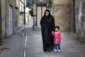 Muslim woman in chador stands in courtyard with little girl.