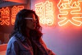 Fashion African girl wears trendy glasses stands near neon sign in night club.