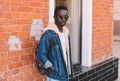Fashion african man wearing jeans jacket, backpack poses on city street Royalty Free Stock Photo