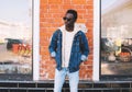 Fashion african man wearing jeans jacket, backpack poses on city street Royalty Free Stock Photo