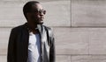 Fashion african man wearing a sunglasses and black rock leather jacket over textured background evening in city Royalty Free Stock Photo
