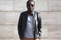 Fashion african man wearing a sunglasses and black rock leather jacket over textured gray background in city Royalty Free Stock Photo